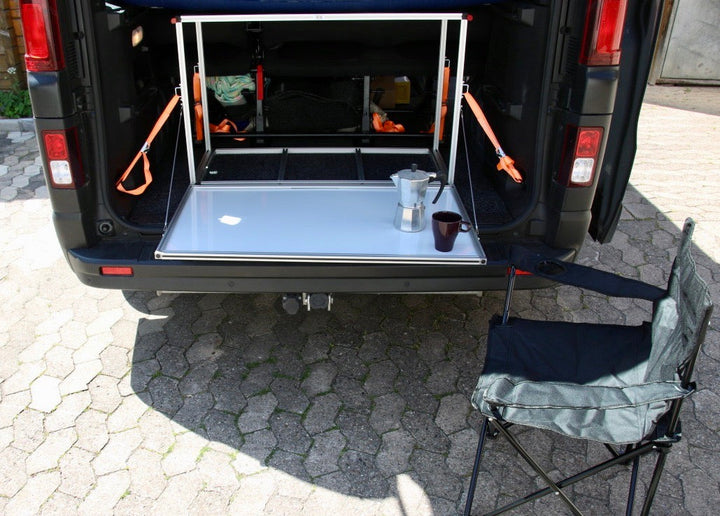 Heckansicht der Campingbox COMO Easy 55 im Opel Movano – mit geöffneter Klappe, Campingstuhl und Kaffeetasse
